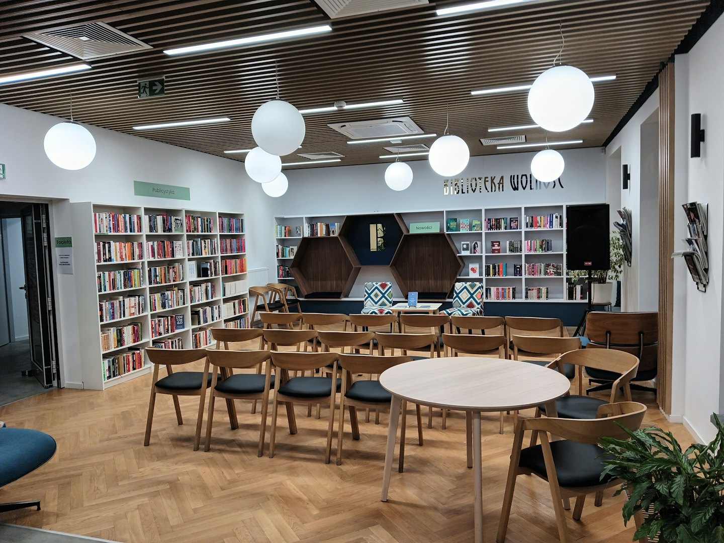 Nowoczesna biblioteka publiczna z drewnianymi stołami i białymi regałami.