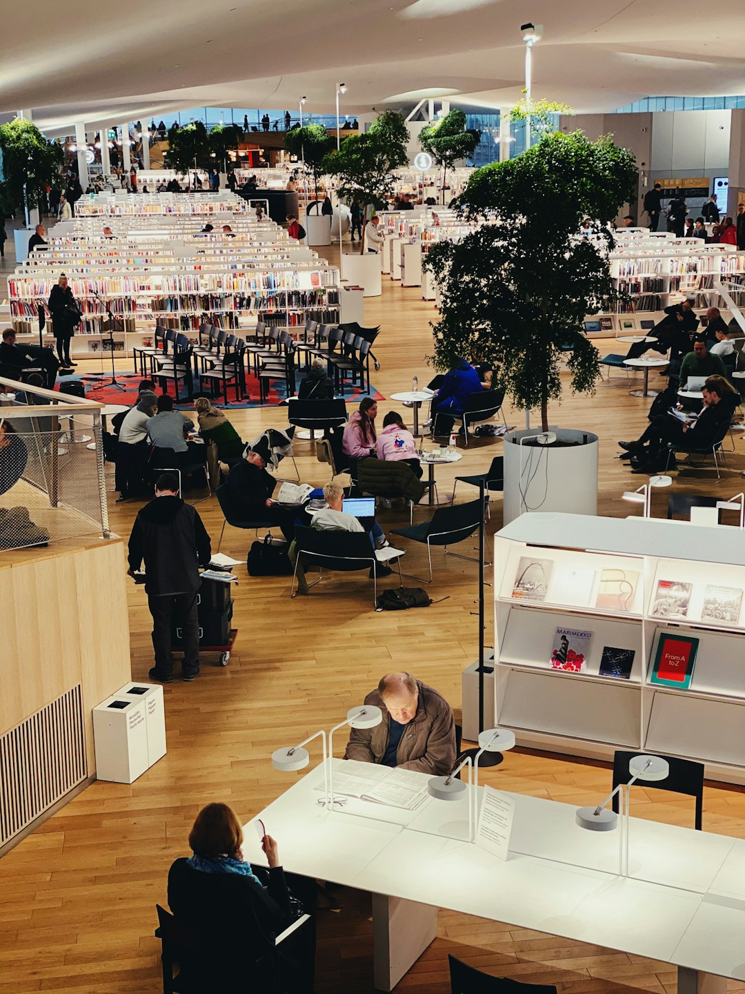 Ludzie czytający i pracujący w jasnej, nowoczesnej, wielopoziomowej bibliotece.