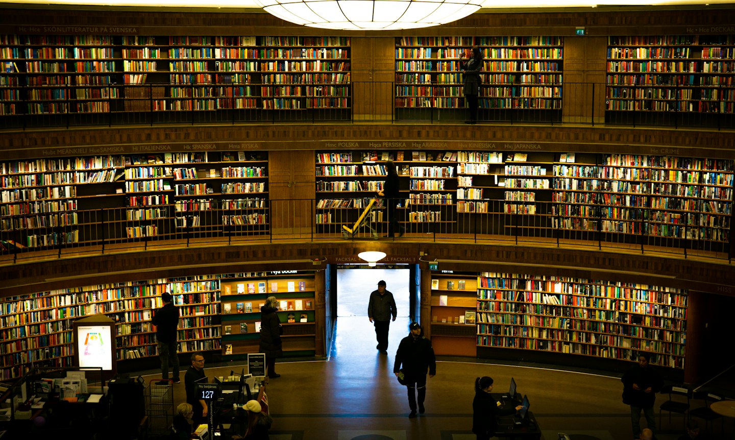 Klienci przeglądają książki w wielkiej, wielopiętrowej bibliotece o okrągłym kształcie.